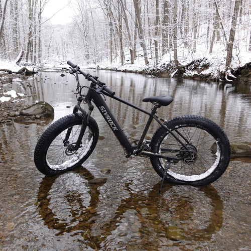 SIVROCK V1 Shimano electric bike parked by a snowy creek, showcasing its fat tires and rugged design.