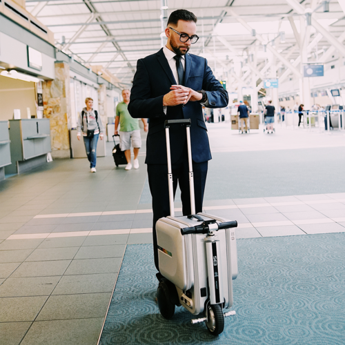 Businessman checking watch with a smart electric suitcase scooter at the airport.